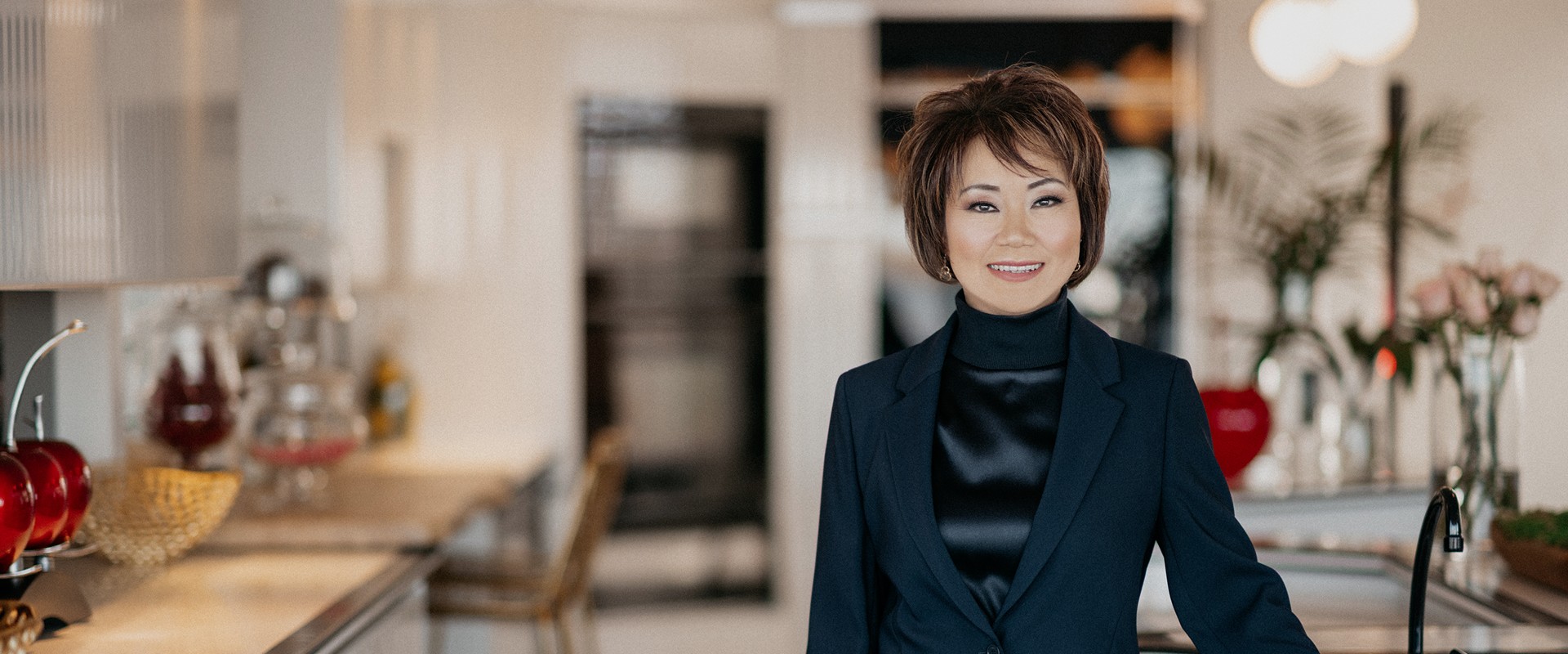 Professional woman in navy blazer and black turtleneck smiling in modern office setting.